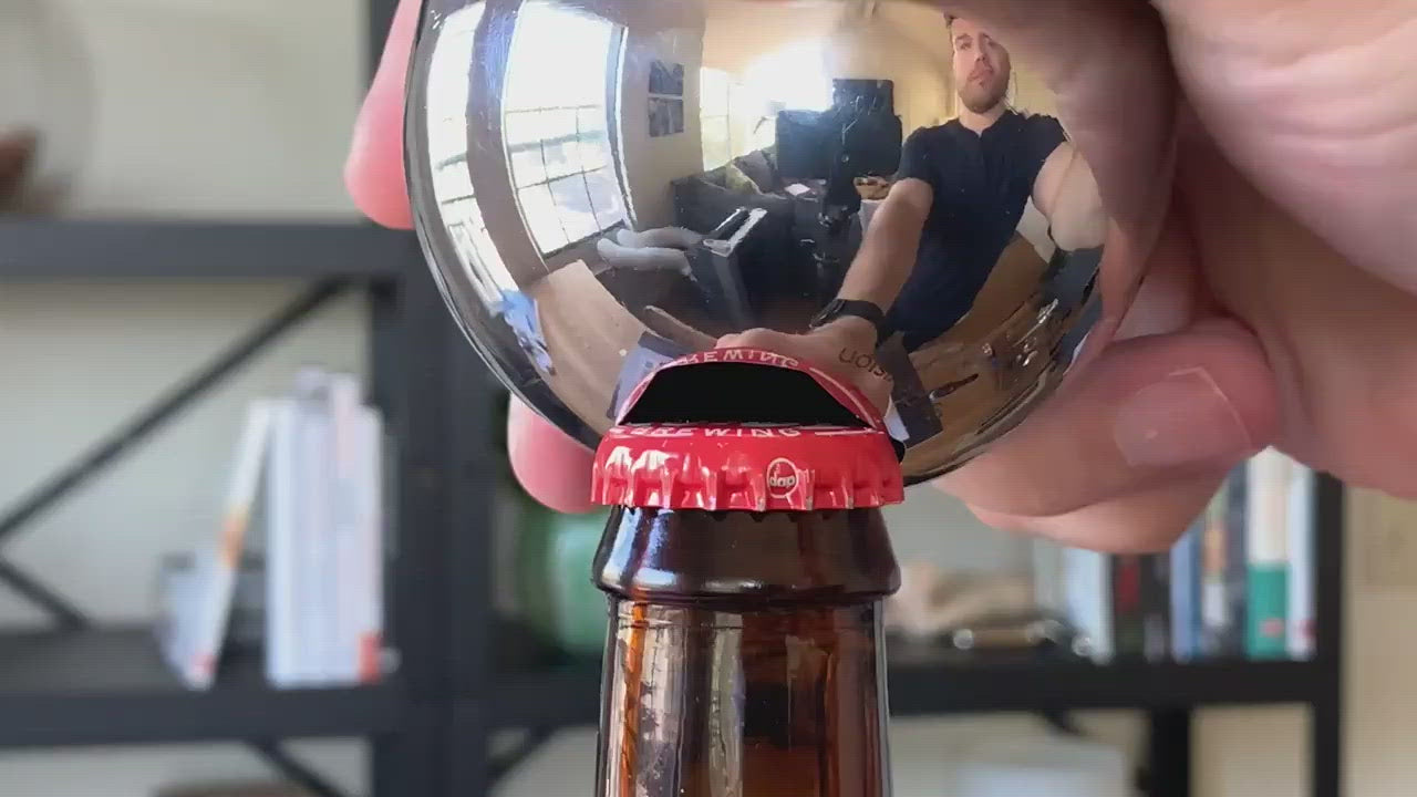 Revision Sainless Steel Convex Bottle Opener prying red cap off of bottle.